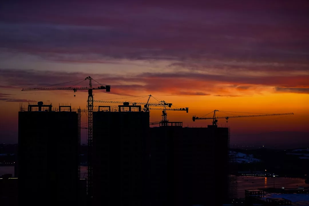 Silhouettes of construction cranes and buildings are visible against an orange and purple sunset sky, capturing the dynamic energy of real estate development.