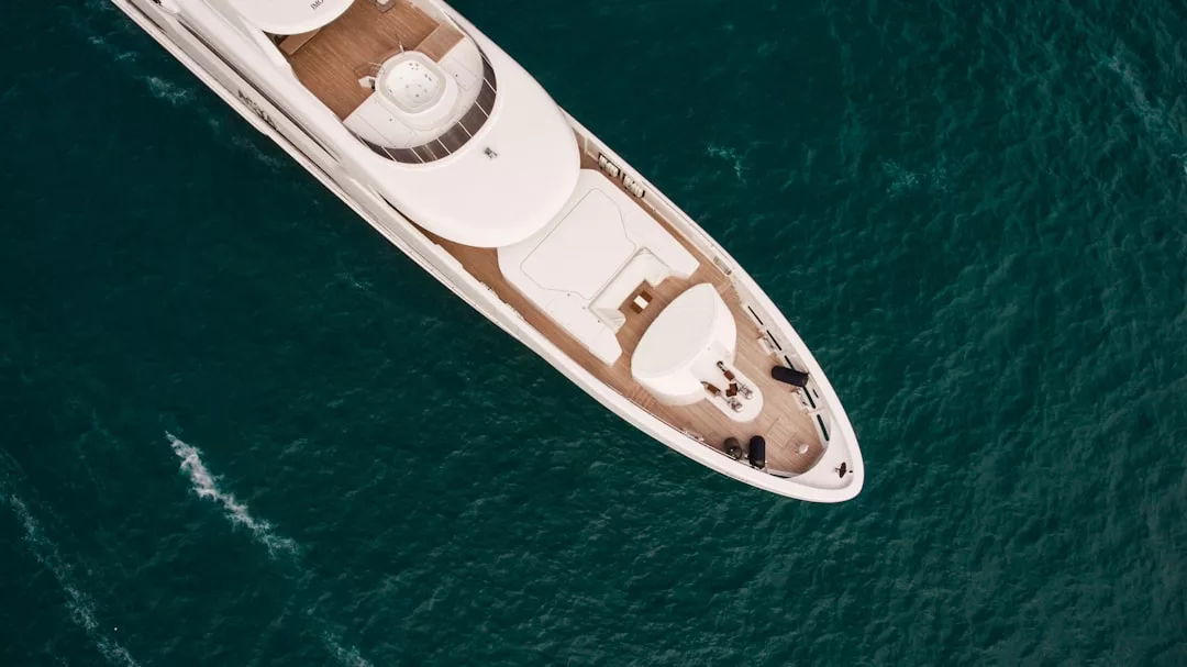 Aerial view of a white luxury yacht cruising on teal ocean water, showcasing the allure of upscale real estate and lifestyle.