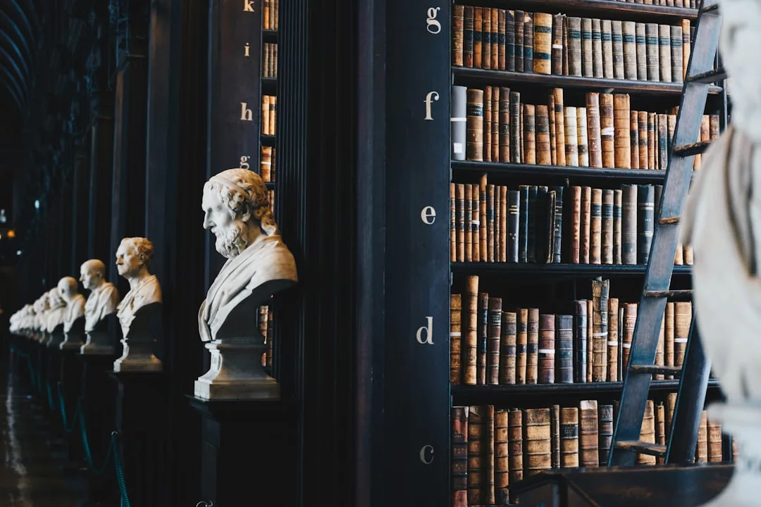 A row of marble busts lines a corridor next to tall bookshelves filled with old books and a wooden ladder—echoing the gravitas of legal aspects in a historic library.