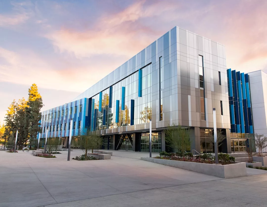 Modern three-story real estate building with reflective blue and silver panels, large windows, and landscaped surroundings, photographed at sunset.