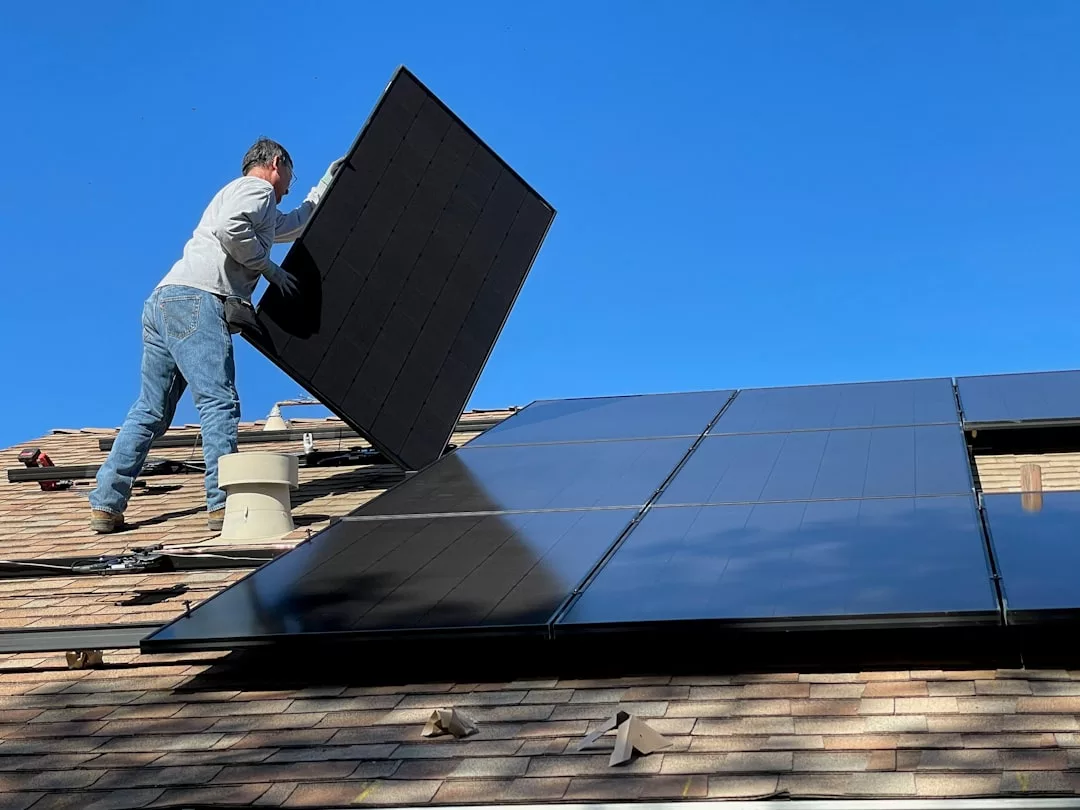 A person installs a solar panel on a residential rooftop, enhancing the property's real estate value, next to several already mounted panels under a clear blue sky.