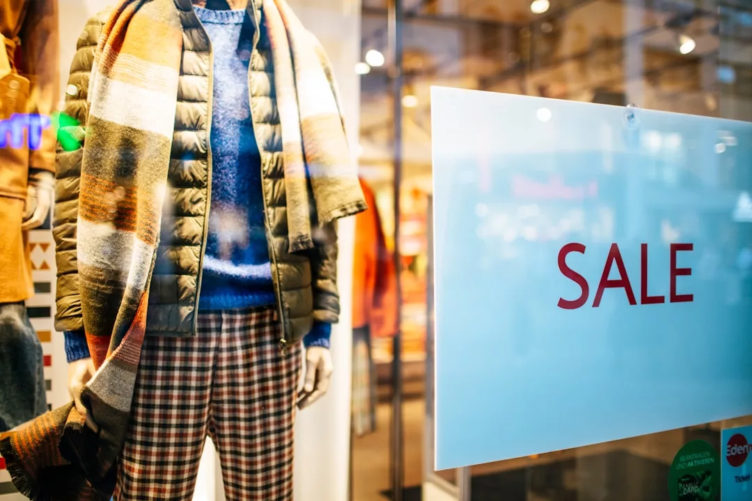 Storefront mannequin dressed in a scarf, puffer jacket, sweater, and plaid pants stands beside a large glass window with a "SALE" sign displayed—perfect style inspiration for shoppers exploring nearby real estate.