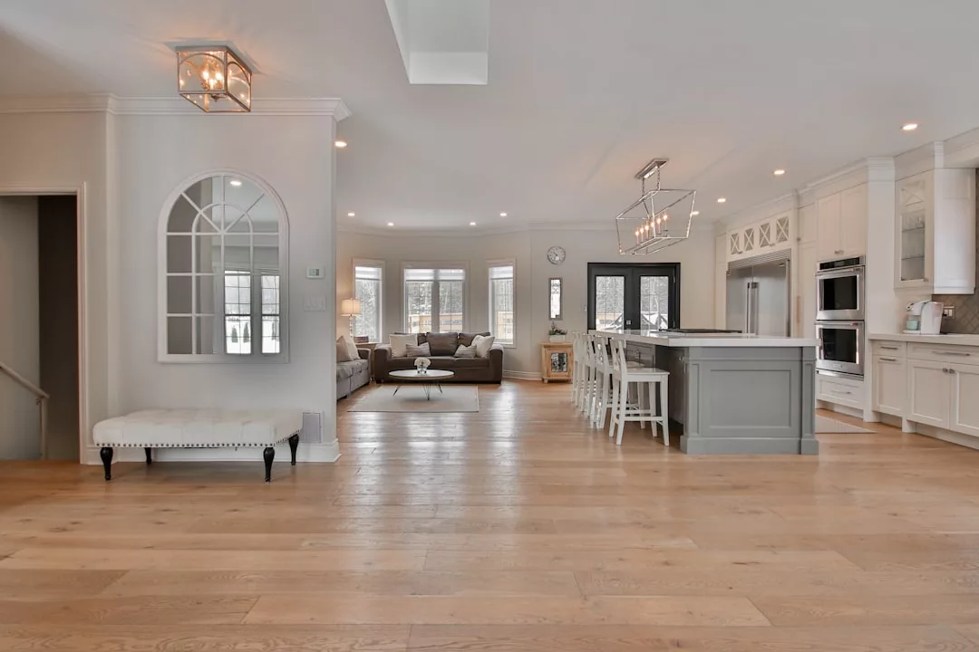 Spacious, modern open-concept kitchen and living area featured in this real estate gem, with light wood floors, a large island, white cabinets, and a cozy sitting area by expansive windows.