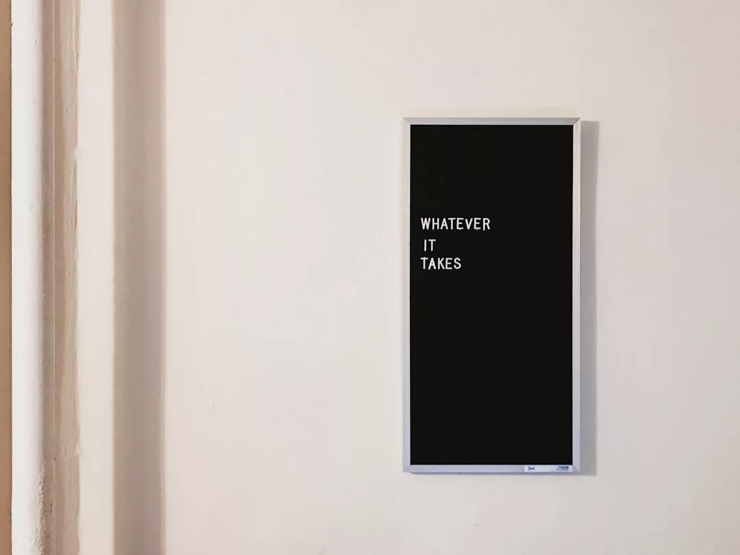 A black rectangular sign on a white wall displays the words “WHATEVER IT TAKES” in white capital letters, reflecting the drive and determination essential in real estate success.