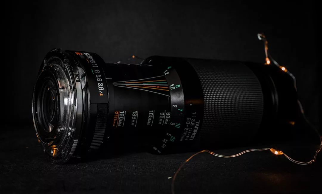 A close-up photo of a black camera lens placed on its side against a dark background, with small string lights next to it—perfect for capturing striking real estate photography.