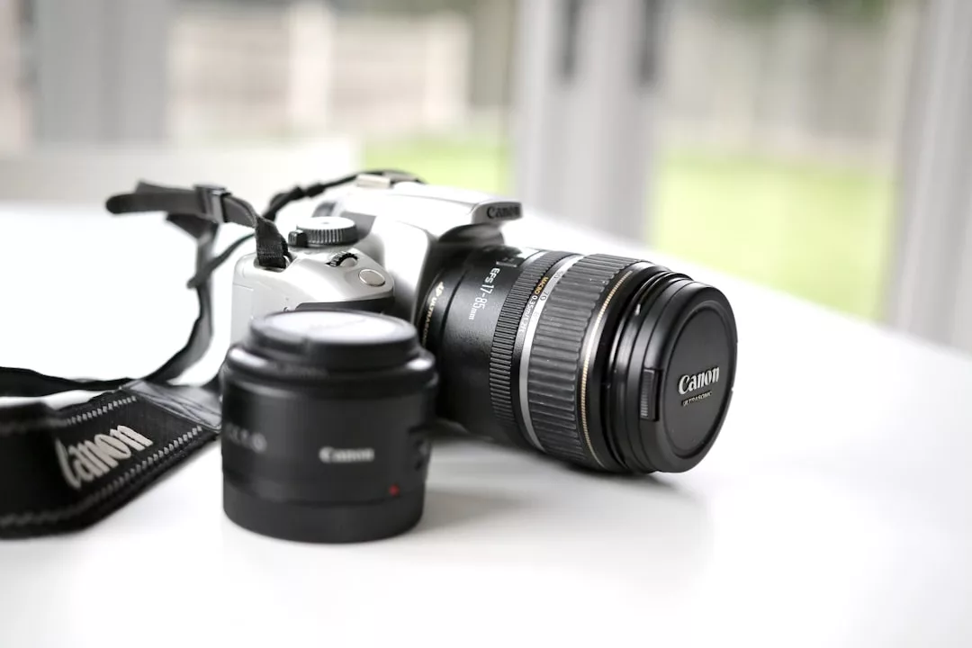 A Canon DSLR camera with a zoom lens attached and a separate prime lens next to it, perfect for real estate photography, placed on a white surface with a blurred background.