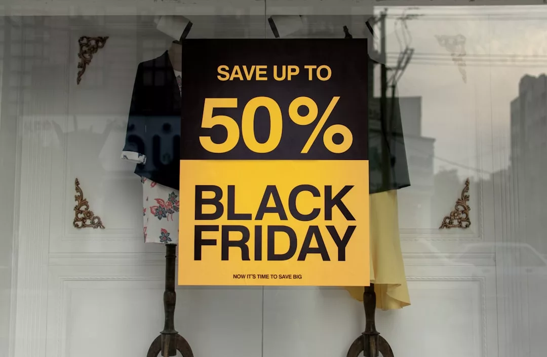 A large sign in a store window reads "Save up to 50%. Black Friday. Now it's time to save big on Real Estate deals" in bold yellow and black text.