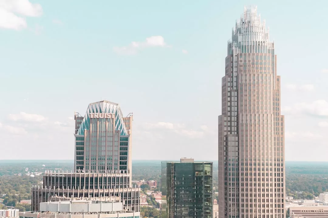 Two tall office buildings, one labeled "Truist," stand side by side against a clear sky, showcasing the city's thriving real estate landscape with greenery visible in the background.