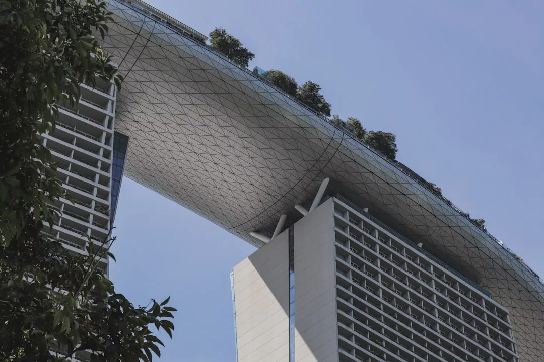 A modern real estate marvel, this building features two towers connected by a large, elevated platform adorned with trees and greenery, set against a clear blue sky.