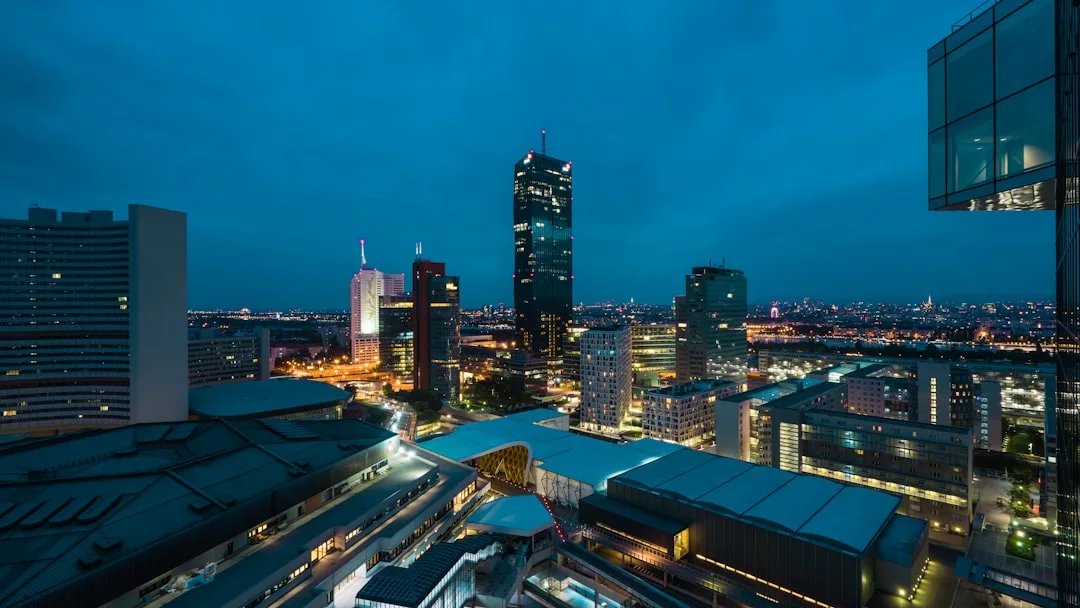 Cityscape at dusk with illuminated skyscrapers and buildings, featuring a prominent tall tower in the center—a stunning view showcasing prime real estate opportunities against a clear, darkening sky above.