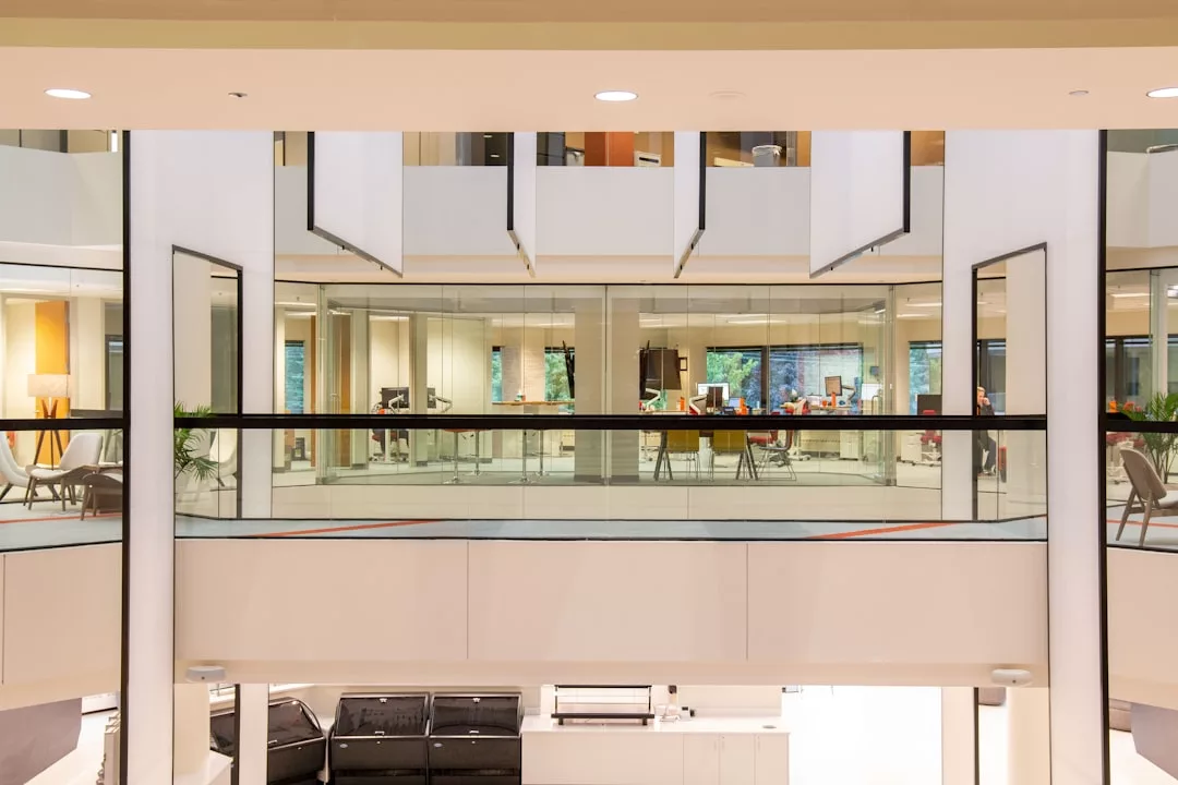 A modern office interior in Oslo with glass walls, open workspaces, and reflections of desks and chairs; ideal for real estate agencies or buyers seeking a stylish work environment. Plants and lamps are visible in the background.