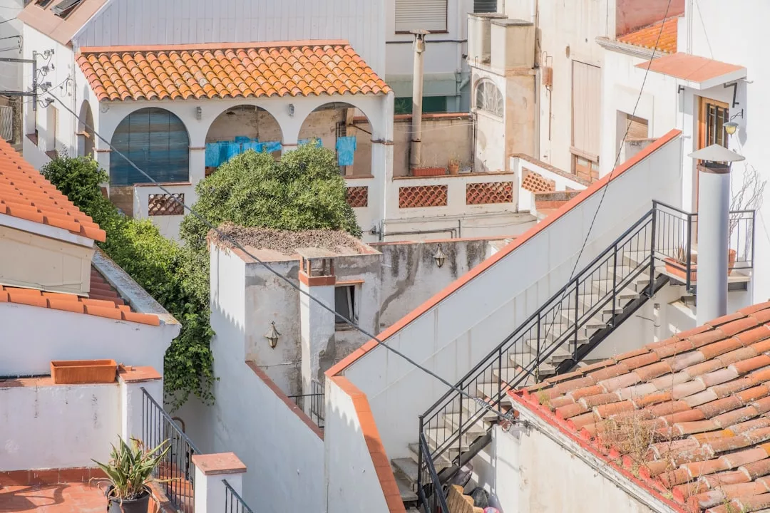 Rooftop view of several white buildings with red-tiled roofs, outdoor staircases, and a small tree in a courtyard area—perfect for Real Estate enthusiasts seeking charm and character.