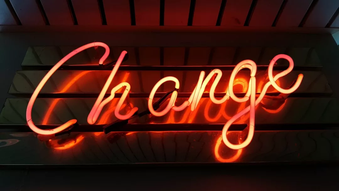 A neon sign displays the word "Change" in cursive orange-red letters against a dark background, hinting at exciting new opportunities in real estate.