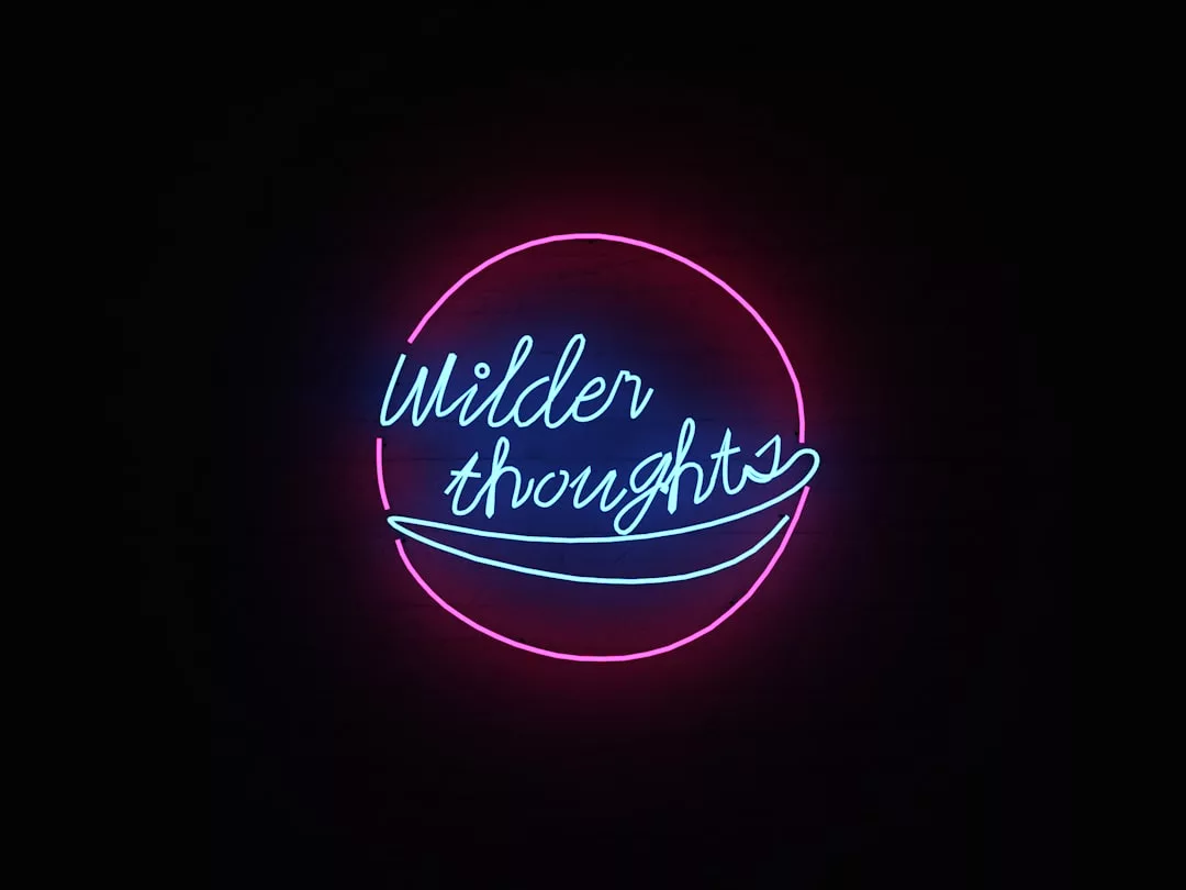 Neon sign with the words "Wilder thoughts" in blue script inside a pink circular outline on a black background—an eye-catching piece perfect for modern real estate offices or stylish property listings.