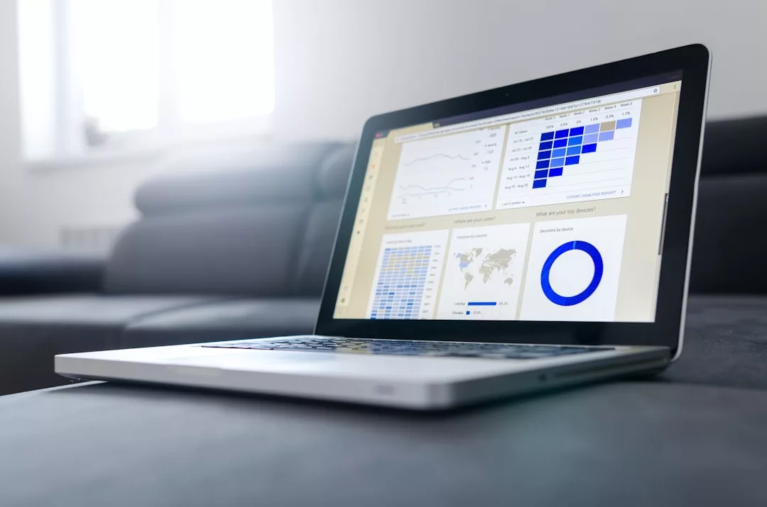 A laptop on a sofa displays real estate data analytics dashboards with charts, graphs, and maps on the screen in a home setting.