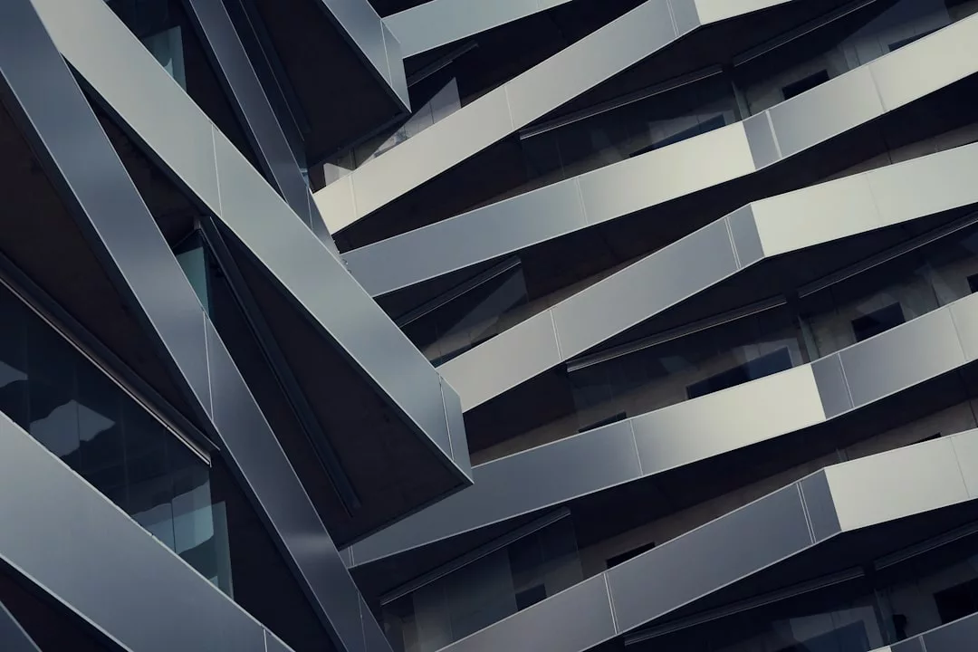 Close-up view of a modern real estate building facade featuring overlapping diagonal metal beams and glass panels.