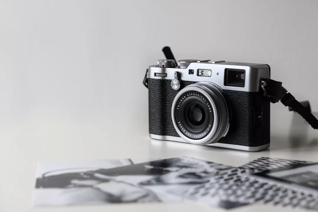 A vintage-style camera rests on a white surface beside two black-and-white real estate photographs placed partially out of focus in the foreground.