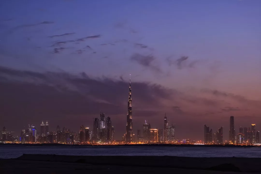 City skyline at dusk with tall buildings, including a prominent Real Estate skyscraper, illuminated against a twilight sky with scattered clouds.