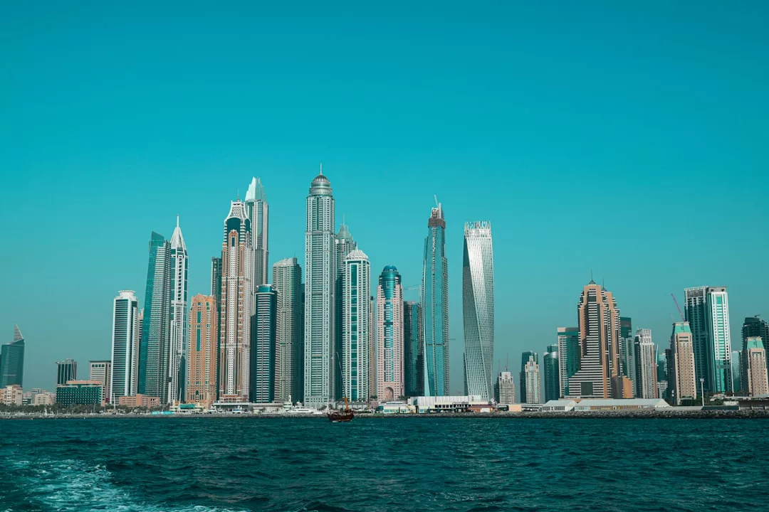 A city skyline featuring numerous modern skyscrapers stands along the waterfront under a clear blue sky, highlighting the area’s thriving real estate landscape.