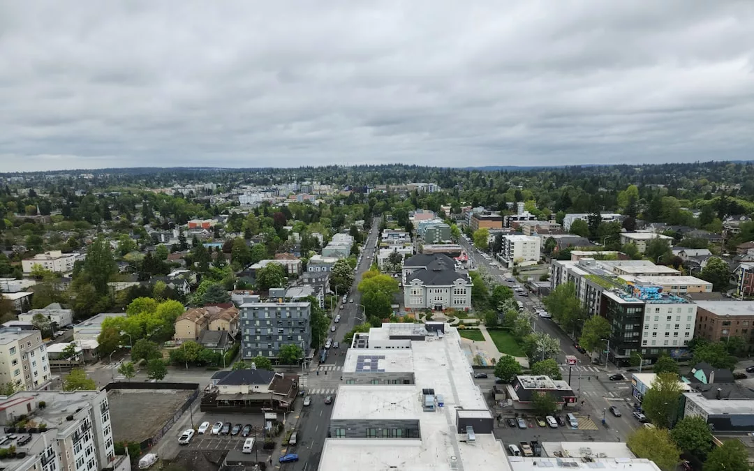 Aerial view of a cityscape featuring low-rise buildings, streets, parked cars, and trees under a cloudy sky—an ideal scene for real estate opportunities.
