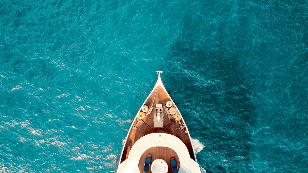 Aerial view of the bow of a yacht cutting through clear blue ocean water, capturing the luxury lifestyle often associated with premier real estate.